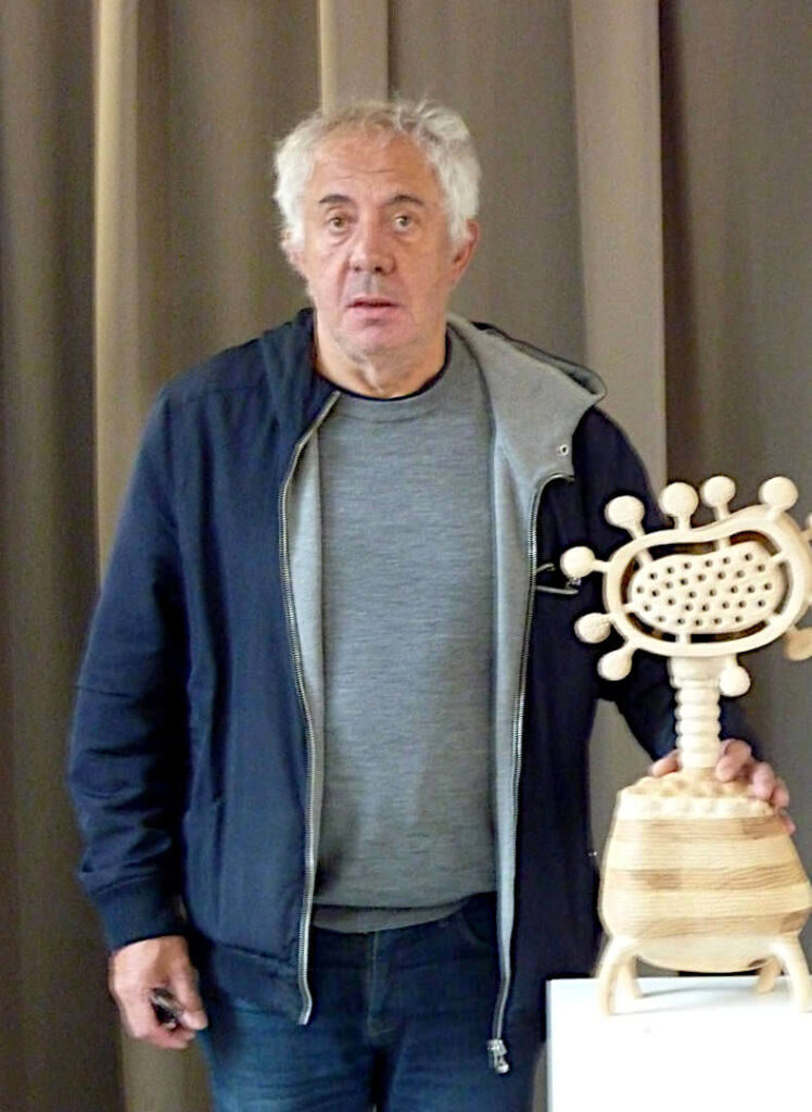 Portrait de l'artiste François LACOSTE, une main posée sur l'une de ses sculptures en bois