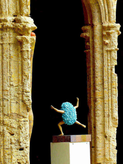 Une énergie en bleu - François LACOSTE Sculpture en bois : bras et jambes émergeant d'un nuage de perles bleues s'élançant sous l'arche antique d'un bâtiment ancien