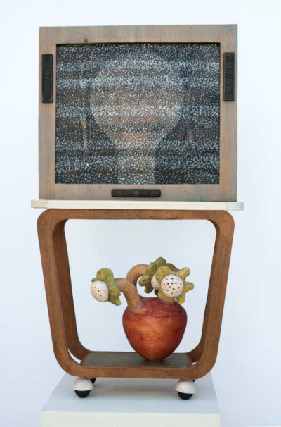Ecran plasma - François LACOSTE Sculpture en bois : tête pixelisée dans une télévision posée sur une console à roulette.