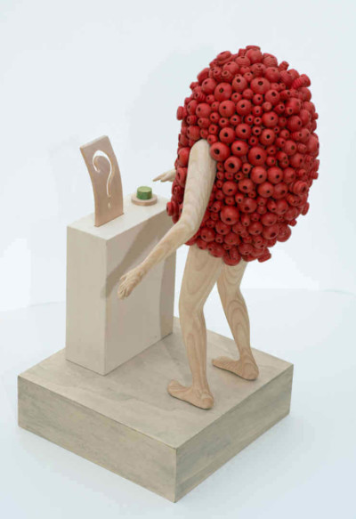 On est en droit de se poser des questions - François LACOSTE Sculpture en bois : bras et jambes émergeant d'un nuage de perles rouges prêt à appuyer sur un bouton vert pour répondre à une question
