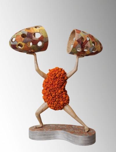 Rapprochements des bords - François LACOSTE Sculpture en bois : bras et jambes émergeant d'un nuage de perles oranges tentant de rapprocher deux pièces d'une même forme au dessus de sa tête
