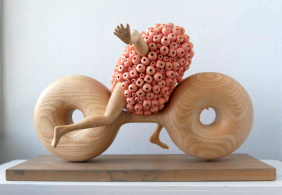 Le régional de l'épate - François LACOSTE Sculpture en bois : bras et jambes émergeant d'un nuage de perles roses se hâtant sur un vélo