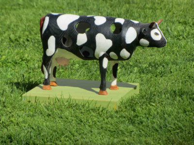 Vache à la double identité connaissant un grand vide intérieur et défendant malgré tout son pré carré - François LACOSTE Sculpture en bois d'une vache noire et blanche, creuse avec des trous au milieu de l'herbe