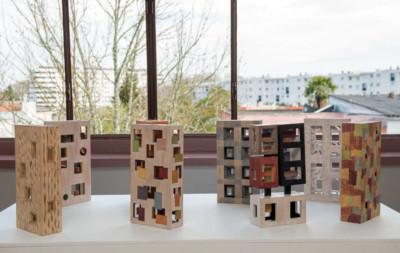 Boîtes Corbu-extrapolations - François LACOSTE 8 sculptures en bois en forme de boîte exposées sur une table devant une fenêtre
