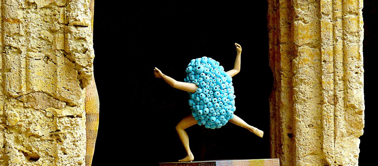Sculpture en bois : bras et jambes émergeant d'un nuage de perles bleues s'élançant entre 2 piliers